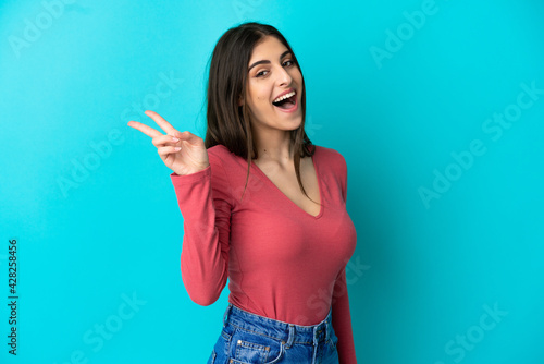 Young caucasian woman isolated on blue background smiling and showing victory sign