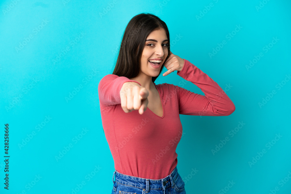 Young caucasian woman isolated on blue background making phone gesture and pointing front Young caucasian woman isolated on blue background making phone gesture and pointing front