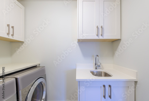 An empty laundry room with cabinet, sink, washer and drier.