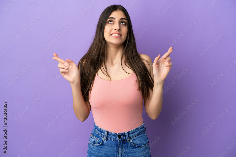 Young caucasian woman isolated on purple background with fingers crossing and wishing the best Young caucasian woman isolated on purple background with fingers crossing and wishing the best