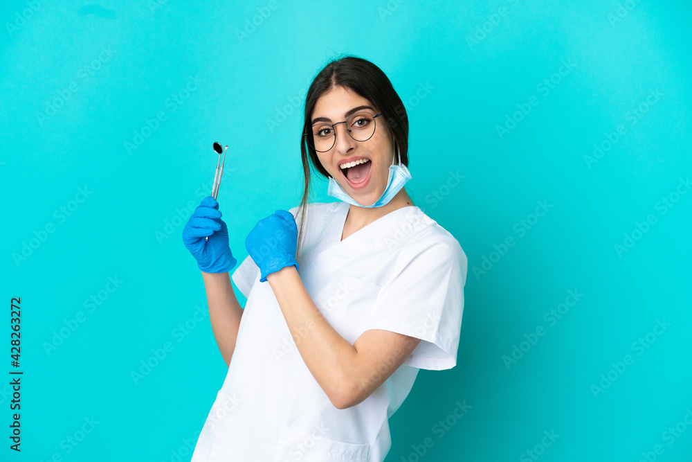Young caucasian dentist woman holding tools isolated on blue background celebrating a victory Young caucasian dentist woman holding tools isolated on blue background celebrating a victory