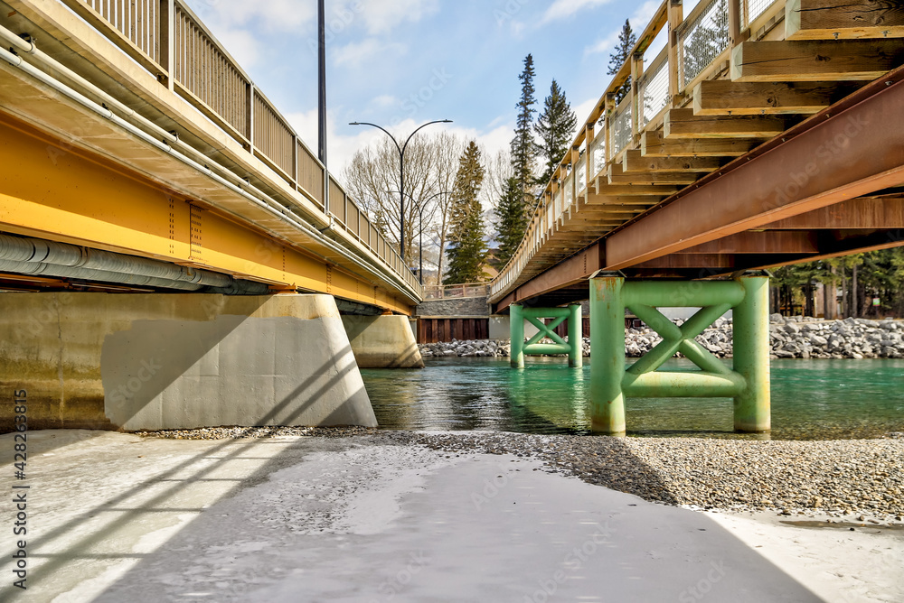 View from below of a pedestrian and traffic bridge side by side over the Bow River in Canmore Alberta View from below of a pedestrian and traffic bridge side by side over the Bow River in Canmore Alberta