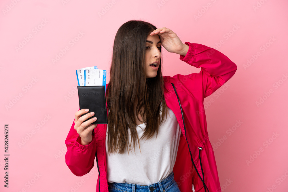 Naklejka premium Young caucasian woman isolated on pink background in vacation with passport and plane tickets while looking something in the distance