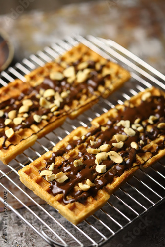 French waffles on a wire rack, drizzled with chocolate and sprinkled with nuts.