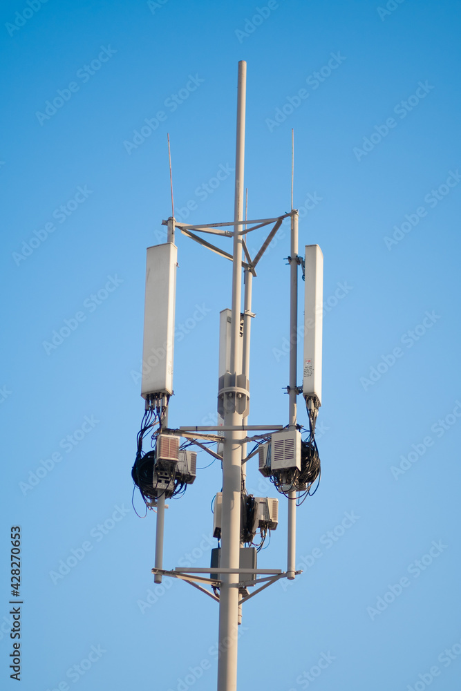 The top of a cell tower pole with antennas on a blue sky background