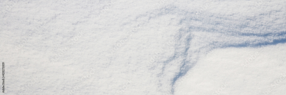 Beautiful winter background with snowy ground. Natural snow texture. Wind sculpted patterns on snow surface. Wide panoramic texture for background and design. Closeup top view with copy space.