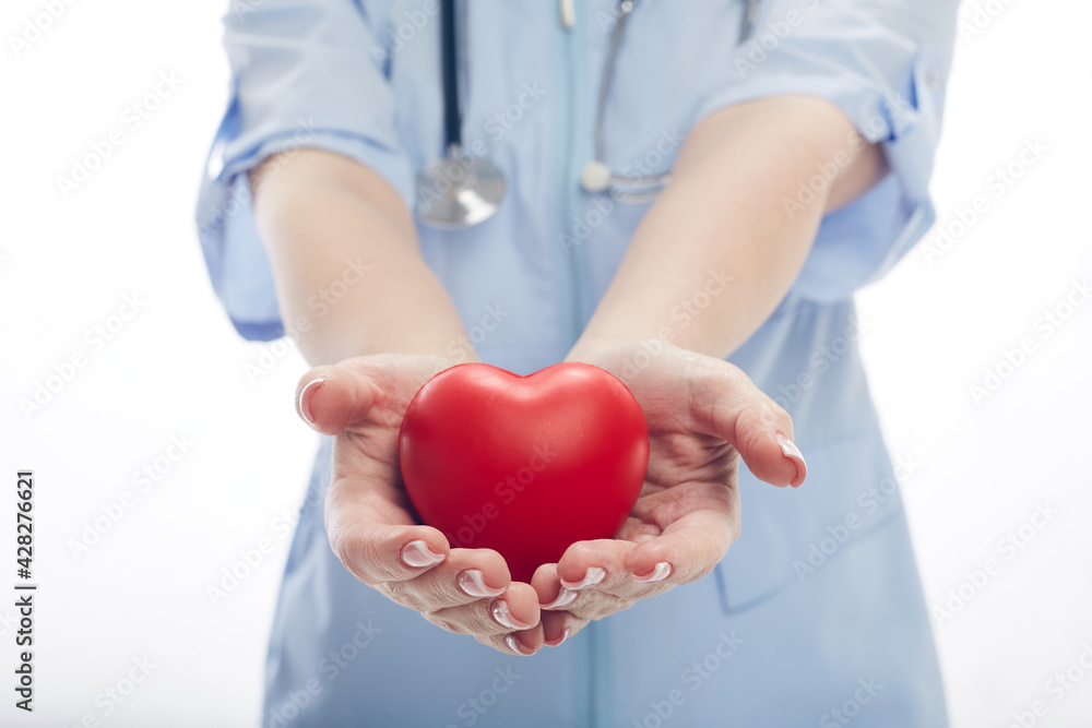 Doctor woman stands in a protective mask with a stethoscope and holds a heart in her hands isolated on white background Doctor woman stands in a protective mask with a stethoscope and holds a heart in her hands isolated on white background