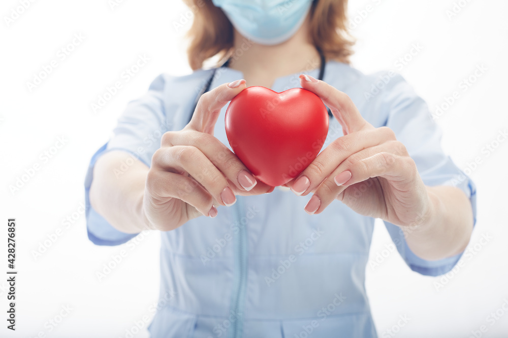 Doctor woman stands in a protective mask with a stethoscope and holds a heart in her hands isolated on white background Doctor woman stands in a protective mask with a stethoscope and holds a heart in her hands isolated on white background
