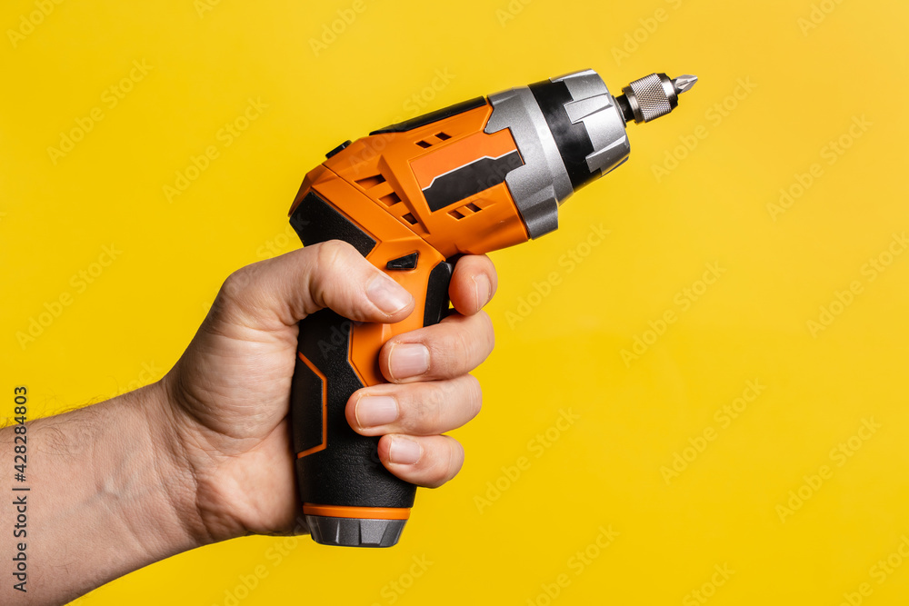 Hand of unknown man holding electric screwdriver - male hold work craft tool on bright yellow background - repair renovation electric equipment tools modern concept