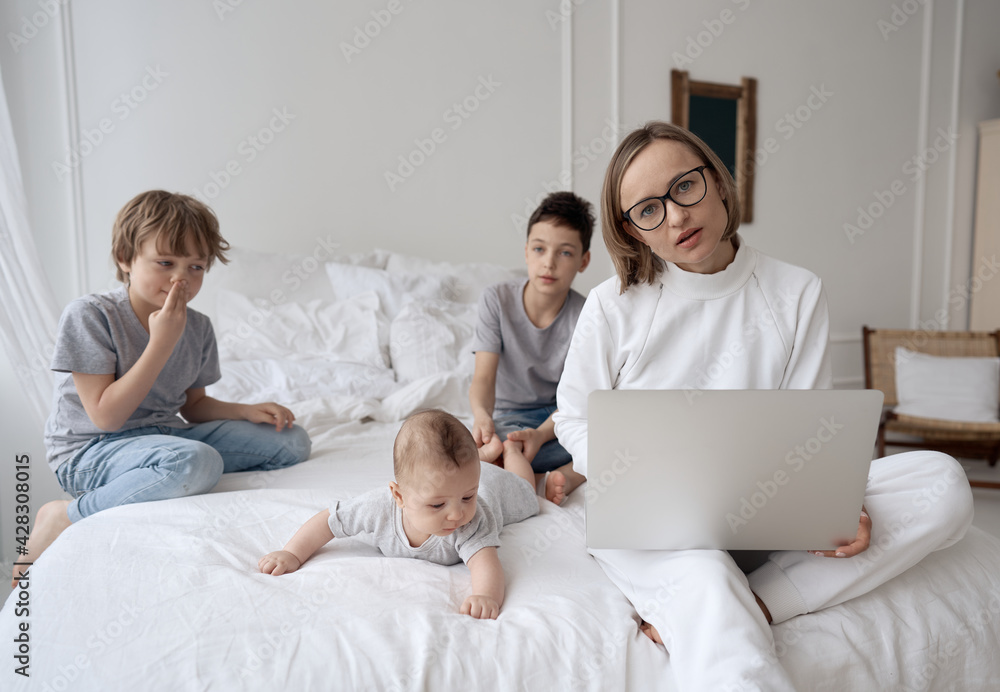 Busy caucasian woman trying to work while baby sitting three kids. Caucasian single mom work from home with the children. High quality photo Busy caucasian woman trying to work while baby sitting three kids. Caucasian single mom work from home with the children. High quality photo