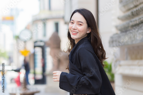 A picture of a beautiful long haired Asian beautiful woman in a black robe smiling happily .walking and looking out in the city outdoors.