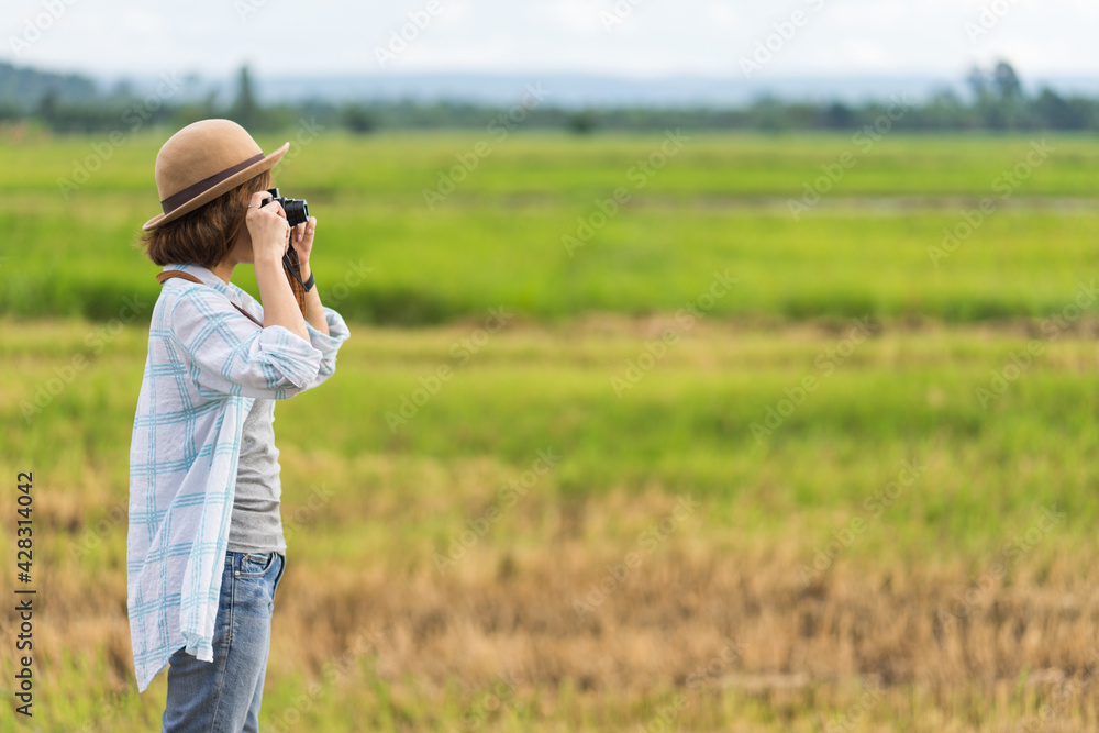 A tourist woman enjoy taking photo of landscape during her summer vacation holiday in the greenery field. A stylish traveler woman in hat taking photo of herself and landscape while relaxing A tourist woman enjoy taking photo of landscape during her summer vacation holiday in the greenery field. A stylish traveler woman in hat taking photo of herself and landscape while relaxing
