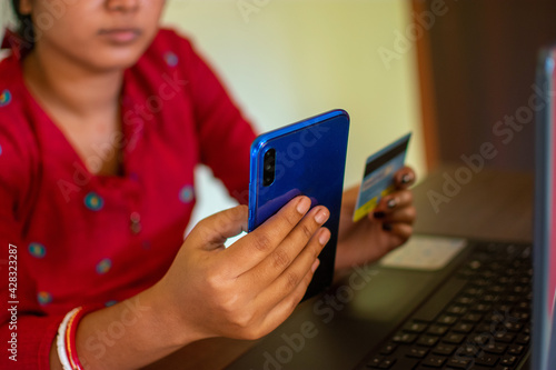 Beautiful Asian / Indian woman holding credit or debit card and mobile phone.Concept of online payment through mobile phone and ATM card.
