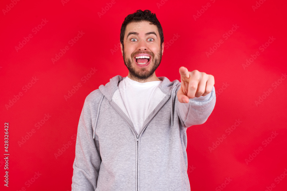 Excited positive young handsome caucasian man in sports clothes against red wall points index finger directly at you, sees something very funny. Wow, amazing Excited positive young handsome caucasian man in sports clothes against red wall points index finger directly at you, sees something very funny. Wow, amazing