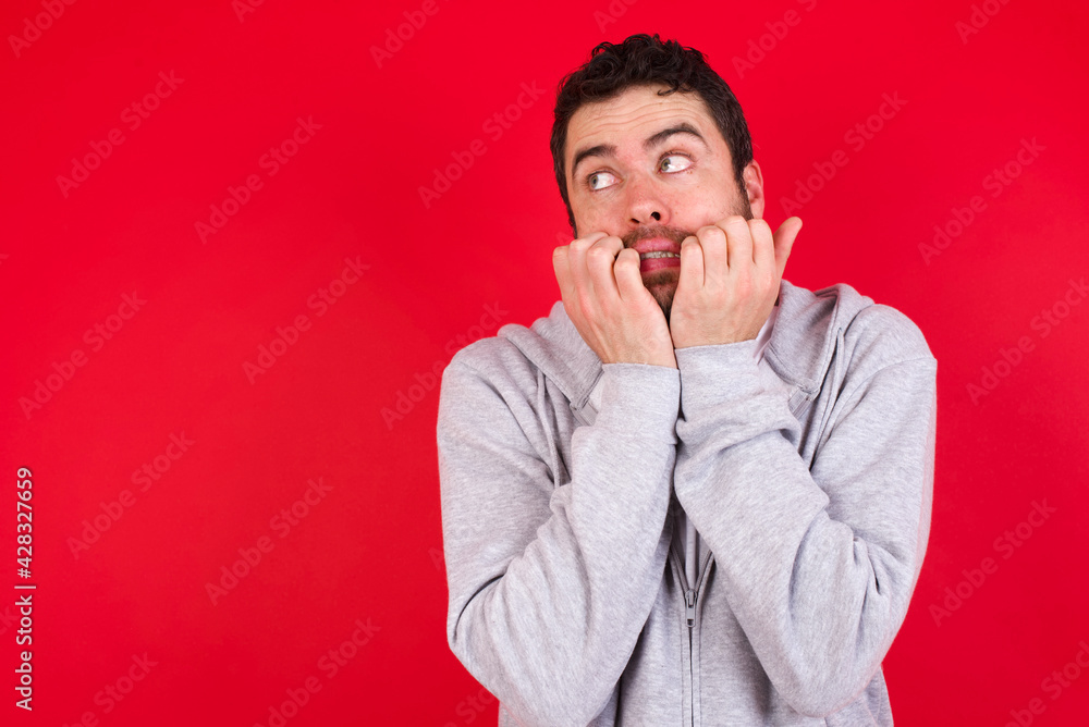 Terrified young handsome caucasian man in sports clothes against red background looks empty space home alone moonless night Terrified young handsome caucasian man in sports clothes against red background looks empty space home alone moonless night