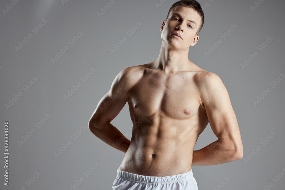 athlete with pumped up abs holding hands behind his back on gray background cropped view close-up