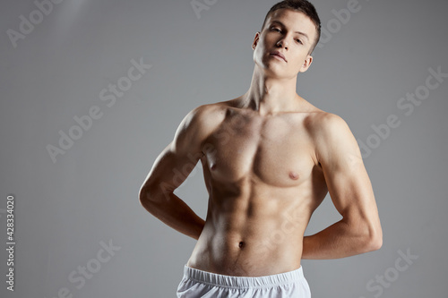 athlete with pumped up abs holding hands behind his back on gray background cropped view close-up