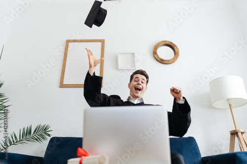 Education, graduation and people concept - happy male student with diploma and laptop at home showing his emotions
