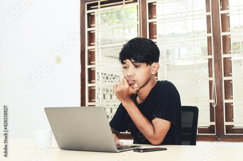 An Asian man sitting in front of a laptop is working on an assignment
