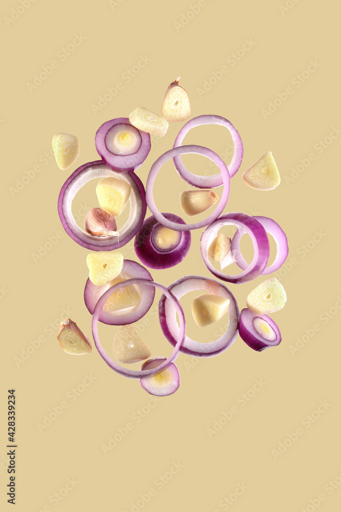 flying onion rings and sliced garlic cloves isolated on a beige background. flying onion rings and sliced garlic cloves isolated on a beige background.