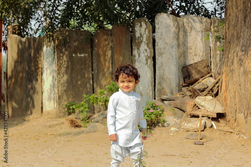 An Indian child smiling at the camera standing in front of the courtyard outside .