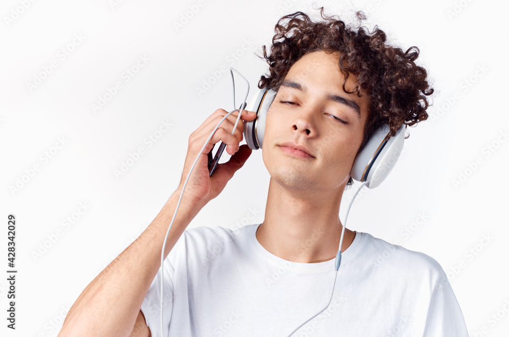 Obraz premium emotional man with curly hair and in headphones listens to music light background