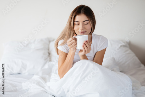 Relaxed woman in bed enjoying the smell of morning coffee