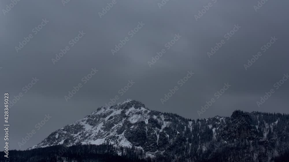 Dense clouds over a rocky snowy peak. Windy winter weather. Clouds and fog with fast movement, .Dark atmosphere before the storm. Dusk over the mountains. Dense clouds over a rocky snowy peak. Windy winter weather. Clouds and fog with fast movement, .Dark atmosphere before the storm. Dusk over the mountains.