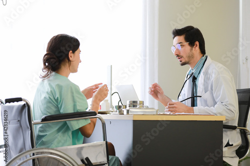 Male medical practitioner in uniform explaining how to eat pills to woman on wheelchair during appointment in modern hospital.