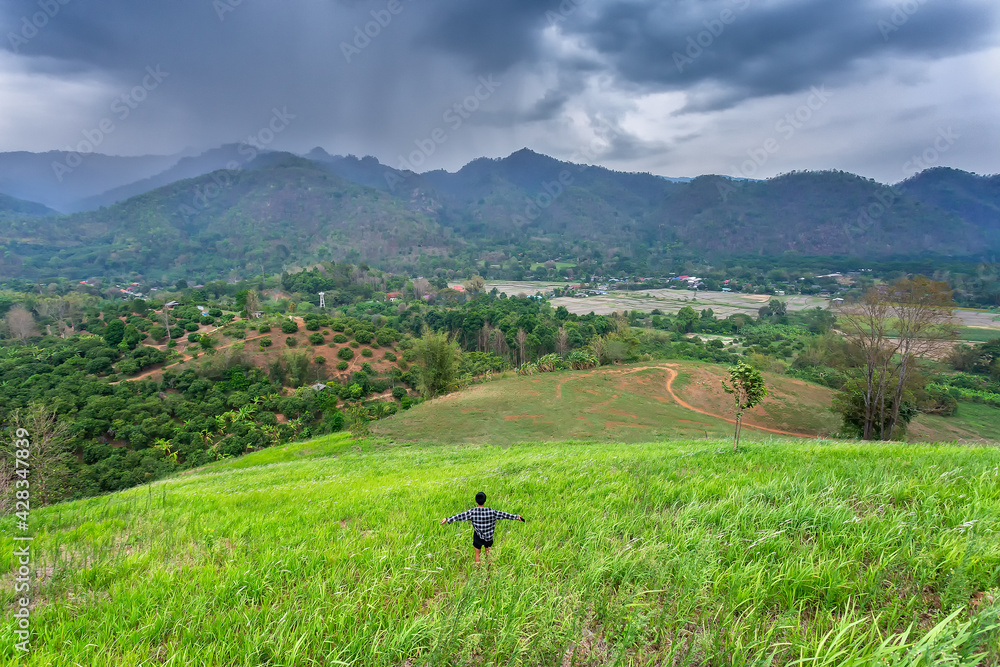Beautiful landscape with mountains And the village in the middle of the mountain, the top was a black cloud, and it was raining on the mountainside. Farmer boy on the hill has a beautiful green meadow Beautiful landscape with mountains And the village in the middle of the mountain, the top was a black cloud, and it was raining on the mountainside. Farmer boy on the hill has a beautiful green meadow