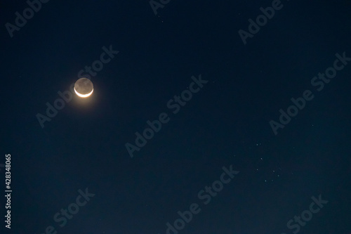 Crescent moon with earthshine is a soft, faint glow on the dark side of the moon and the Pleiades or Seven Sisters in twilight sky. 