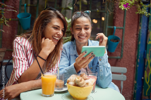 Two female friends enjoying a smartphone content while spending a free time at bar's garden. Leisure, bar, friendship, outdoor