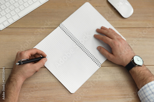 Left-handed man writing in notebook at wooden table, top view photo