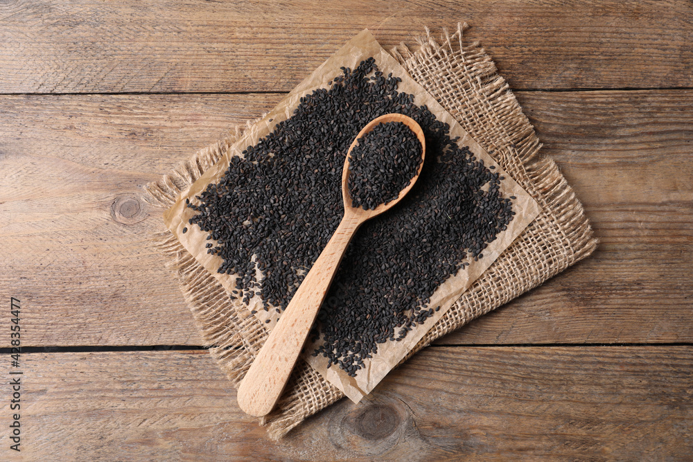 Fototapeta premium Black sesame seeds and spoon on wooden table, flat lay