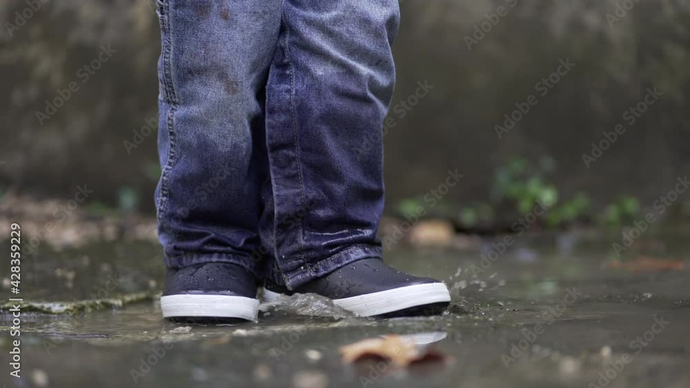 Toddler boy splashes into puddle of water. Child plays with puddles Toddler boy splashes into puddle of water. Child plays with puddles