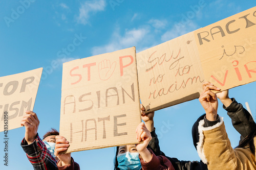 Group of demonstrators protest on the street for equal rights - Asian people demonstrators wearing face masks during stop asian hate campaign - Focus on banners