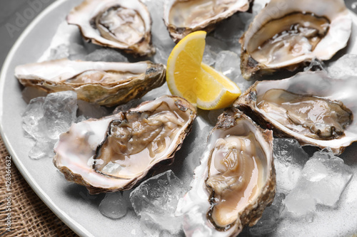 Delicious fresh oysters with lemon slices served on table, closeup