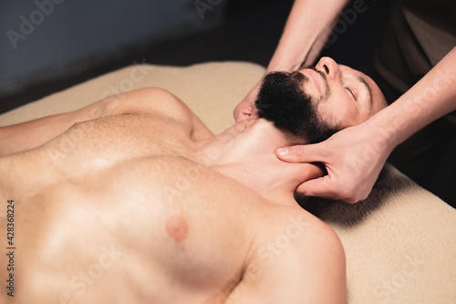 In a professional massage parlor, a Caucasian male athlete with a beard is kneading the neck. Sports massage of the lateral longitudinal muscles of the neck