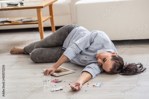 Young woman who overdosed on drugs lying on the floor fainted, holding a picture of a loss person still in her hand