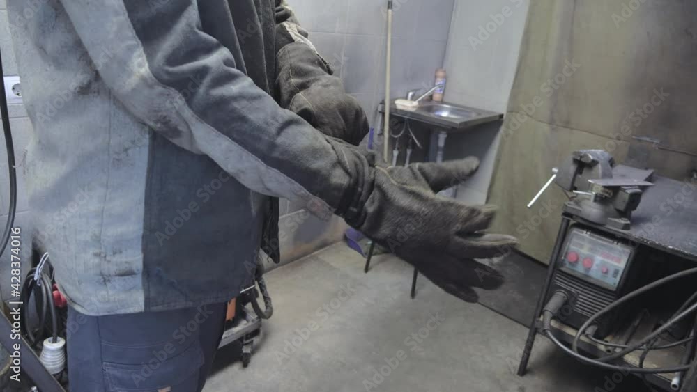 A worker in a workshop puts on protective gloves on his hands. Compliance with workplace safety regulations A worker in a workshop puts on protective gloves on his hands. Compliance with workplace safety regulations