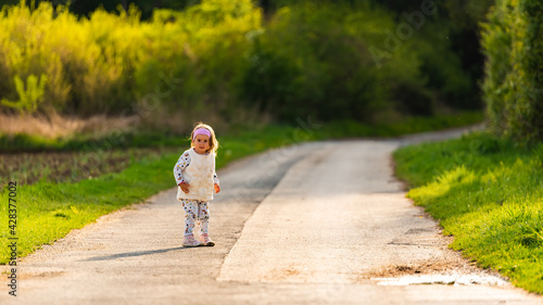 Child on walk outdoors on a rural road leading to forest.