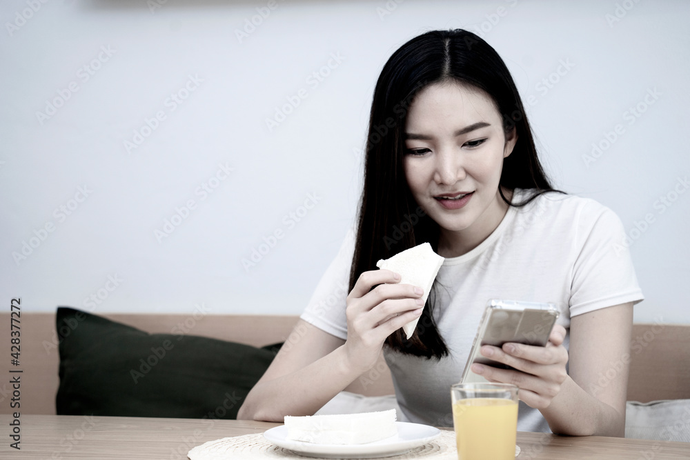 Asian woman eating breakfast with sandwiches and orange juice Asian woman eating breakfast with sandwiches and orange juice
