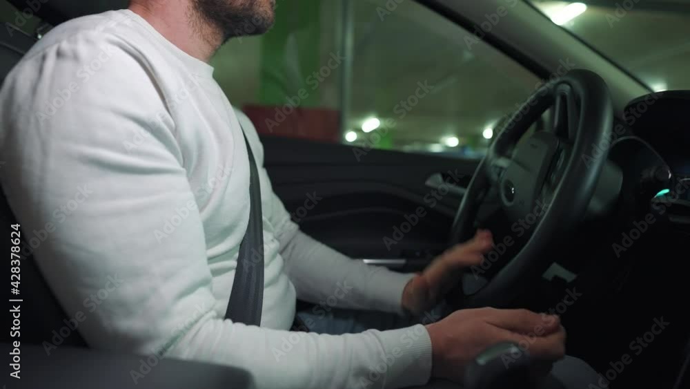 Man driving car through an underground parking lot and is looking for a place to park or drives away. Side view Man driving car through an underground parking lot and is looking for a place to park or drives away. Side view