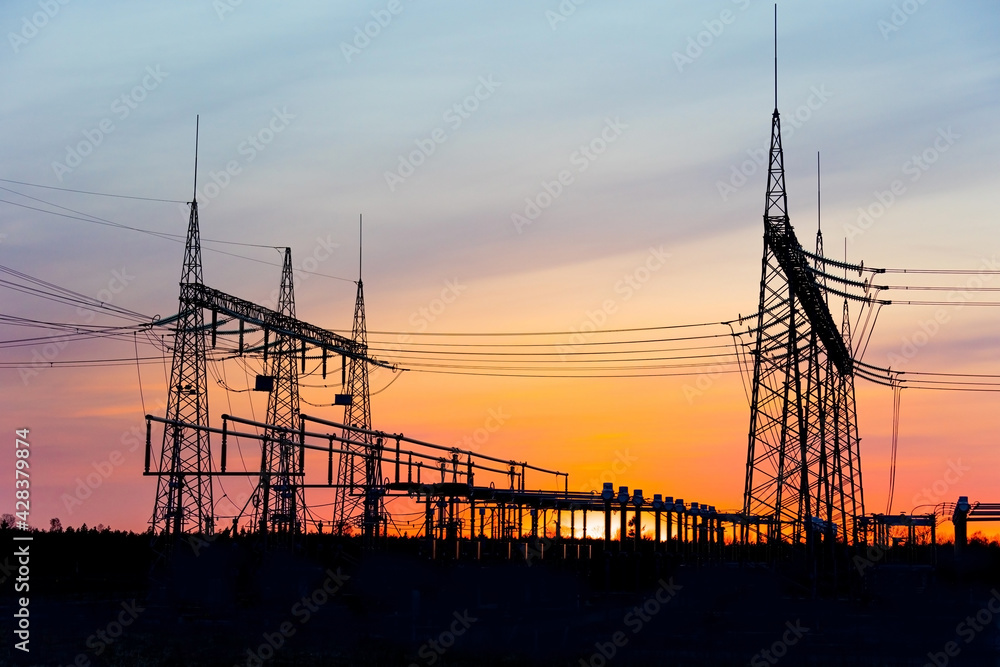 Electricity poles at sunset. High voltage grid towers with wire cable at distribution station.