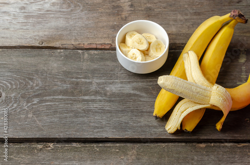 Several bananas and slices in a white plate on a rustic wooden background preparing for cooking with copy space.