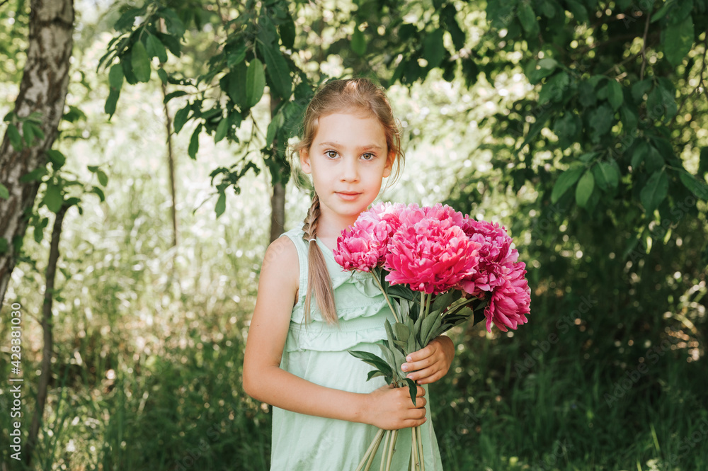 portrait of a happy cute little caucasian seven year old kid girl in light green sundress, holds in hands a bouquet of pink peony flowers in full bloom on the background of nature portrait of a happy cute little caucasian seven year old kid girl in light green sundress, holds in hands a bouquet of pink peony flowers in full bloom on the background of nature