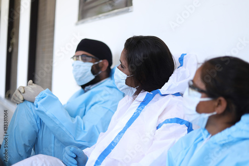 Healthcare workers in hazmat suits taking a rest and sitting at a hallway after a hectic day photo