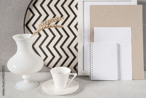 Composition with empty picture frame,notebook,cup of coffee and vase. Elegant working place. Scandinavian interior design.Home office concept.