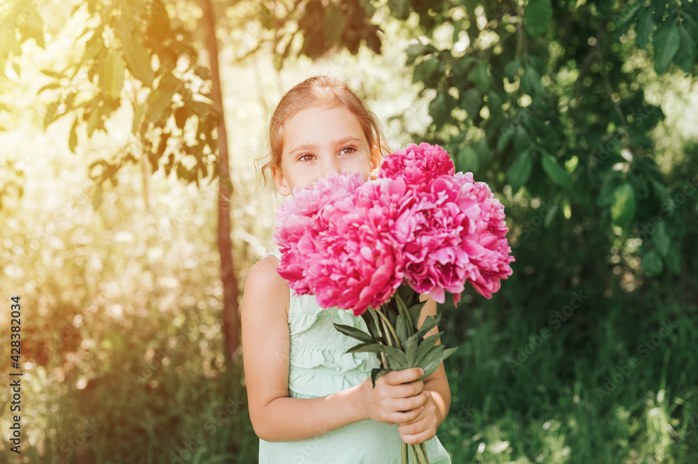 portrait of a happy cute little caucasian seven year old kid girl in light green sundress, holds in hands a bouquet of pink peony flowers in full bloom on the background of nature. flare portrait of a happy cute little caucasian seven year old kid girl in light green sundress, holds in hands a bouquet of pink peony flowers in full bloom on the background of nature. flare