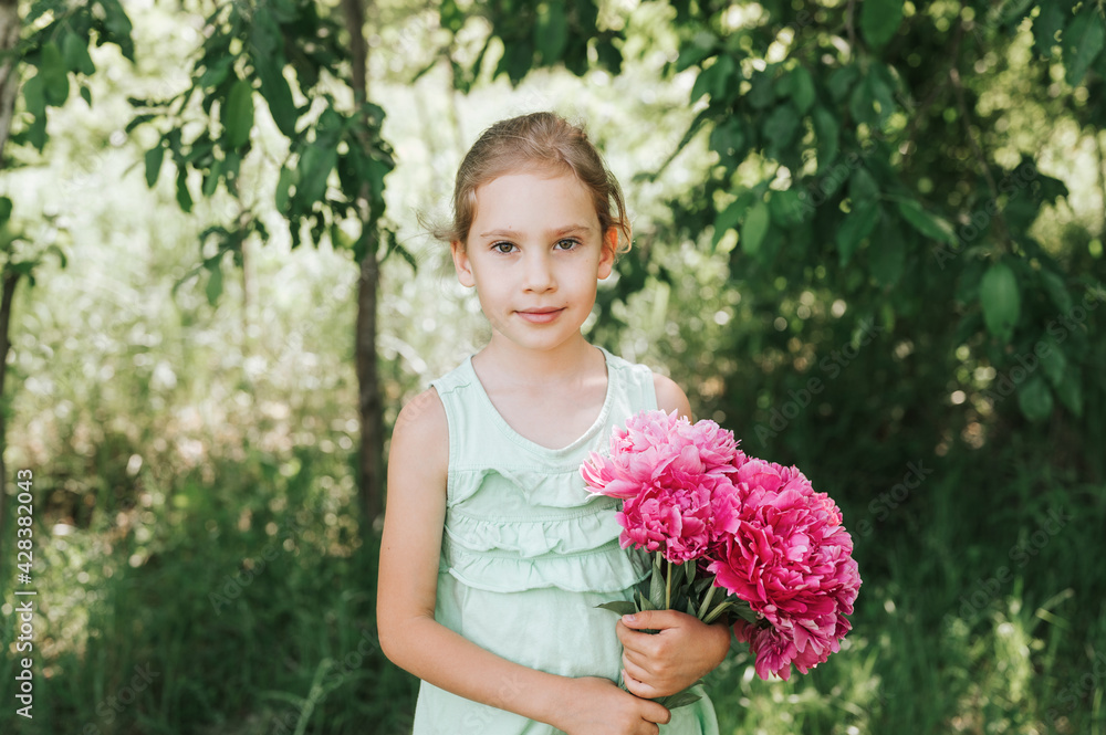 portrait of a happy cute little caucasian seven year old kid girl in light green sundress, holds in hands a bouquet of pink peony flowers in full bloom on the background of nature portrait of a happy cute little caucasian seven year old kid girl in light green sundress, holds in hands a bouquet of pink peony flowers in full bloom on the background of nature
